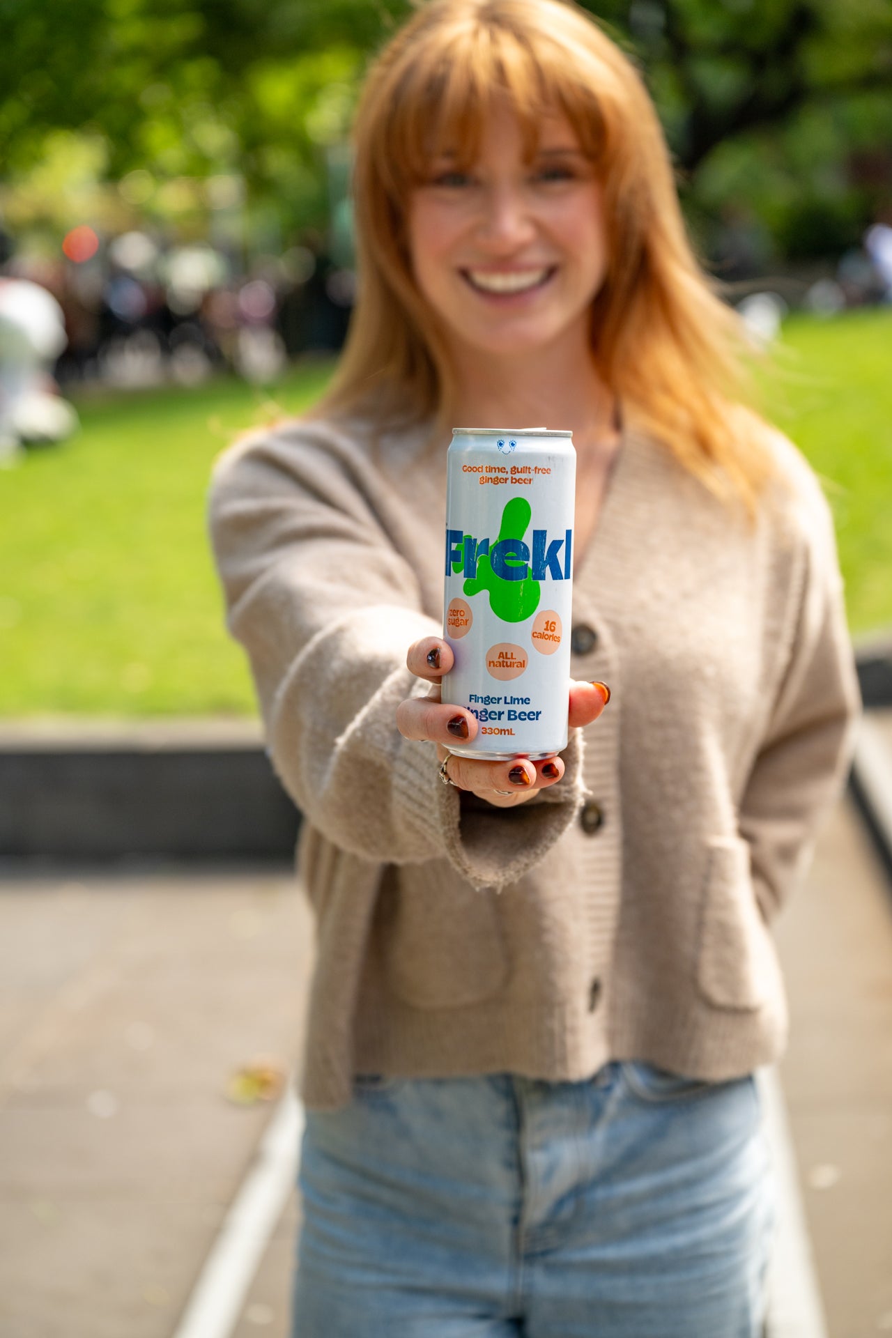 Woman smiling holding a Frekl drink can outdoors
